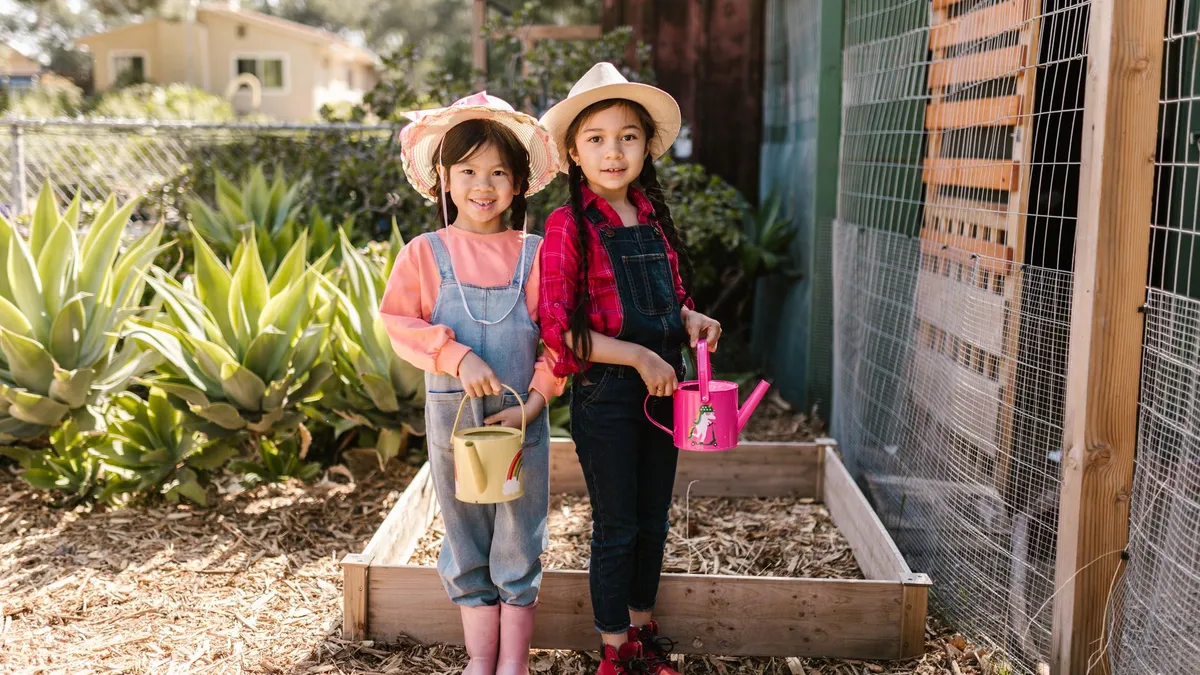 Dues nenes regant plantes en un hort escolar a la primavera