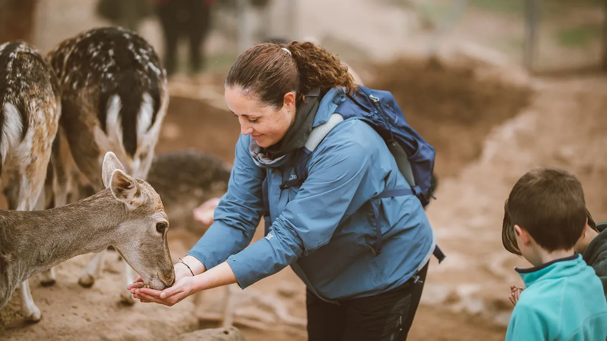 Una dona i un nen alimentant amb calma una daina a Granja Natura, exemple de teràpia assistida amb animals
